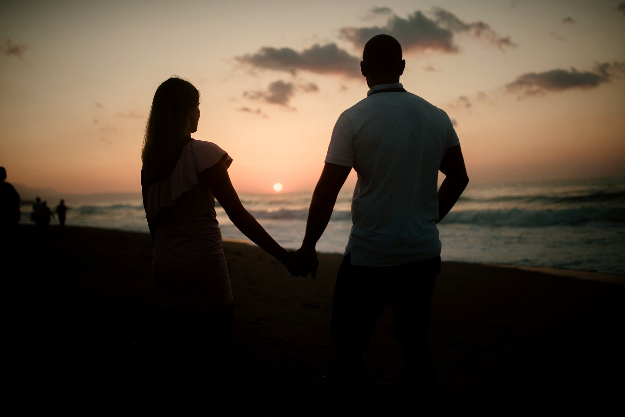 Couple holding hands, silhouetted against the setting sun